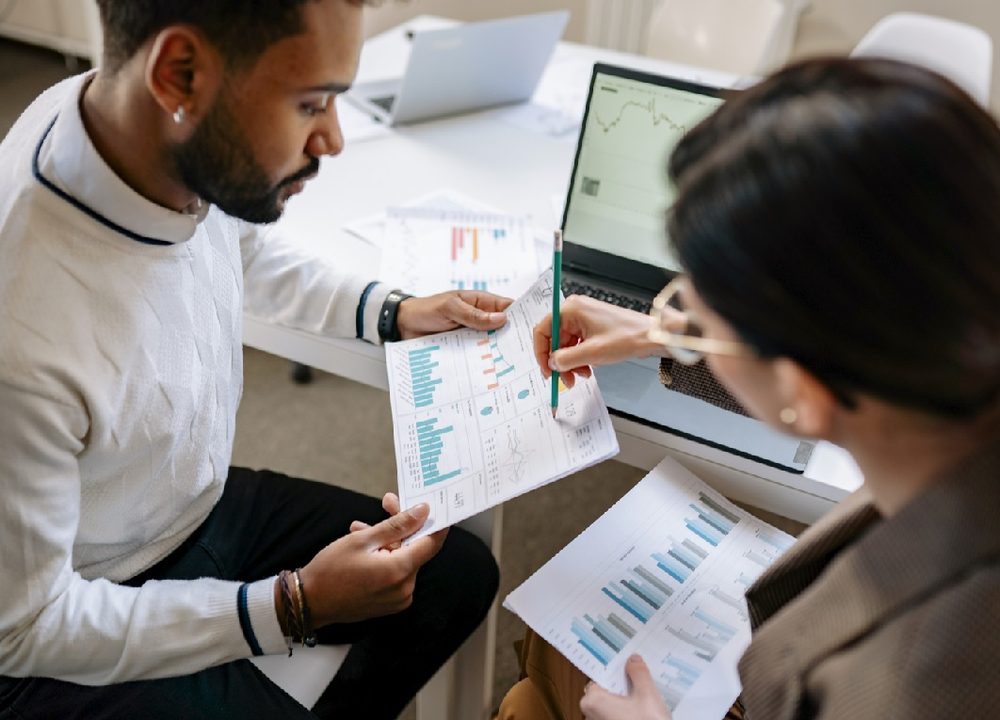 Two analysts reviewing printed charts beside a laptop
